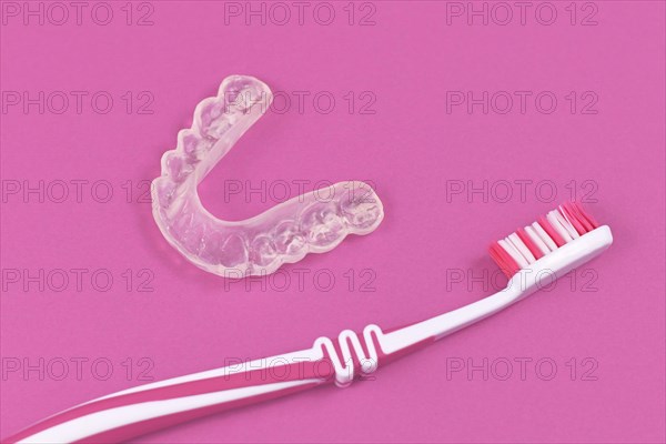 Customized transparent teeth bite guard clear aligners for lower jaw with tooth brush on pink background