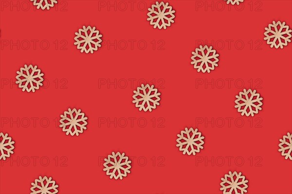 Simple seamless top view flat lay with wooden snowflake ornaments arranged on bright red background