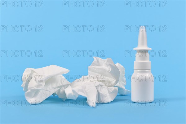 Nasal spray bottle and used tissues used during common cold on blue background