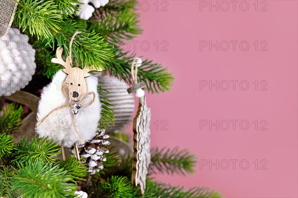 Christmas tree branch with natural sheep ornament made from wood and wool in front of pink background with copy space