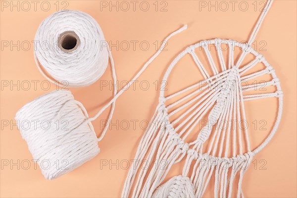 Rolls of cotton macrame cord and finished wall hanging object on beige background