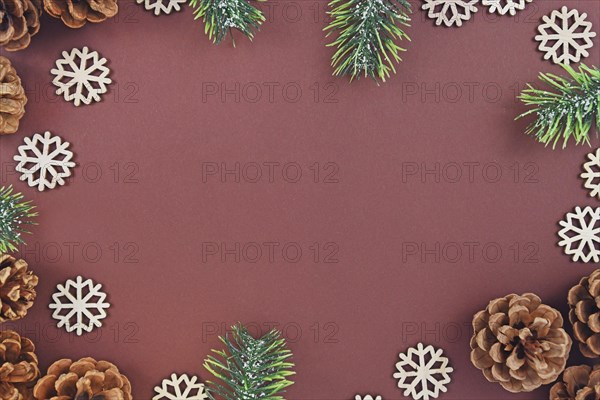 Seasonal Christmas flat lay with pine or fir cones and branches and wooden snowflake ornaments surrounding brown background with empty copy space like a border