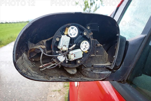 Torn off broken side mirror with glass missing and wires sticking out on red car