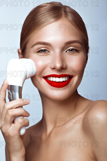 Beautiful girl with red lips and classic makeup with massage brush in hand. Beauty face. Photo taken in the studio