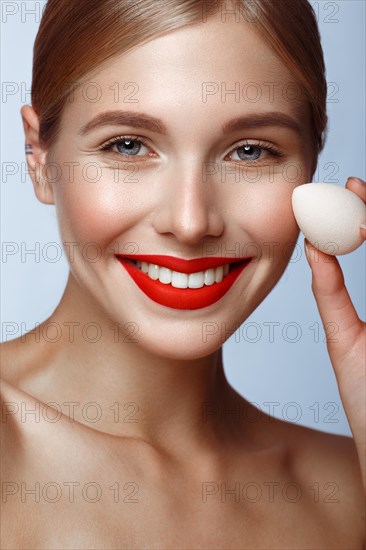 Beautiful girl with red lips and classic makeup with foundation sponge in hand. Beauty face. Photo taken in the studio