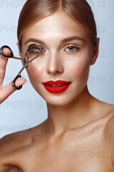 Beautiful girl with red lips and classic makeup with curler in hand. Beauty face. Photo taken in the studio