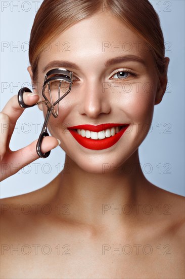 Beautiful girl with red lips and classic makeup with curler in hand. Beauty face. Photo taken in the studio