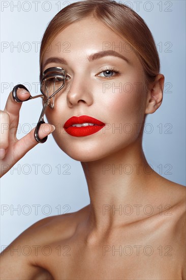 Beautiful girl with red lips and classic makeup with curler in hand. Beauty face. Photo taken in the studio