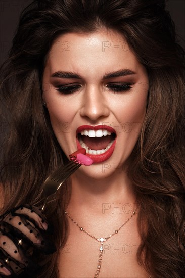 Beautiful girl with red lips and classic makeup and curls with lipstick in hand. Beauty face. Photo taken in the studio