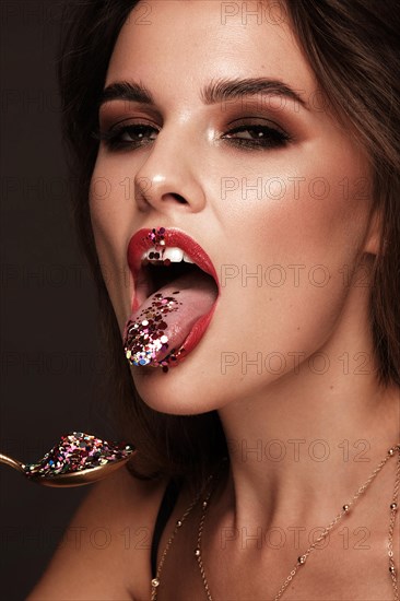 Beautiful girl with red lips and classic makeup and curls with creative glitter. Beauty face. Photo taken in the studio