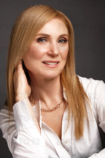 Portrait of a beautiful elderly woman in a white shirt with classic makeup and blond hair