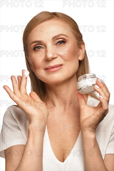 Portrait of a beautiful elderly woman in a white shirt with a moisturizing face cream in her hands