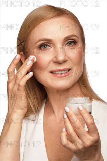 Portrait of a beautiful elderly woman in a white shirt with a moisturizing face cream in her hands