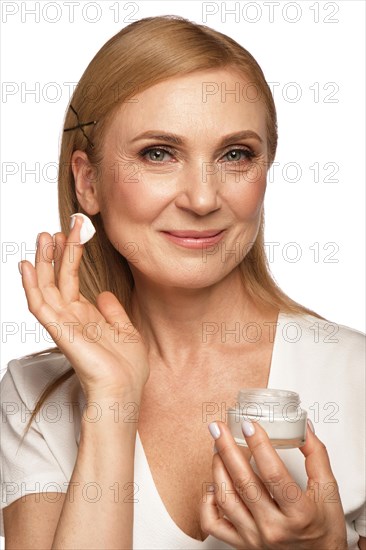 Portrait of a beautiful elderly woman in a white shirt with a moisturizing face cream in her hands