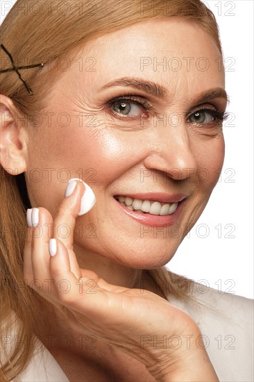 Portrait of a beautiful elderly woman in a white shirt with a moisturizing face cream in her hands