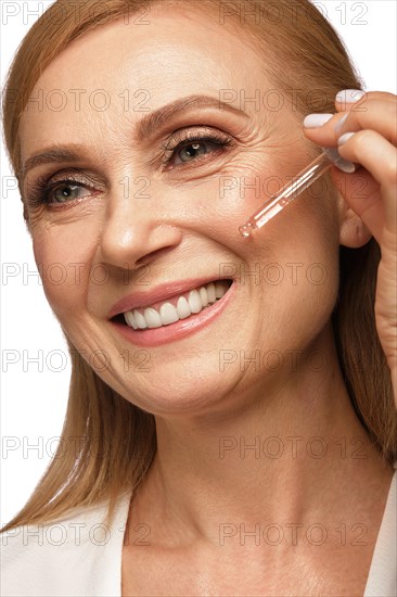 Portrait of a beautiful elderly woman in a white shirt with cosmetic face oil in her hands