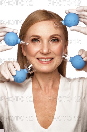 Portrait of a beautiful elderly woman in a white shirt with classic makeup and blond hair with massage tools in her hands