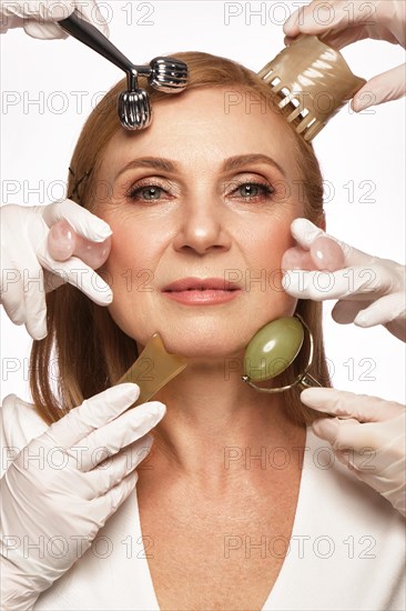 Portrait of a beautiful elderly woman in a white shirt with classic makeup and blond hair with massage tools in her hands