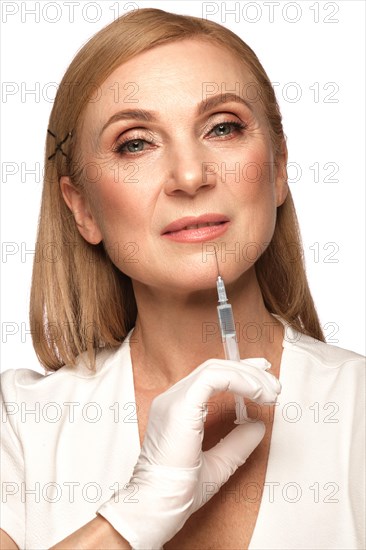 Portrait of a beautiful elderly woman in a white shirt with classic makeup and blond hair with syringe in her hands