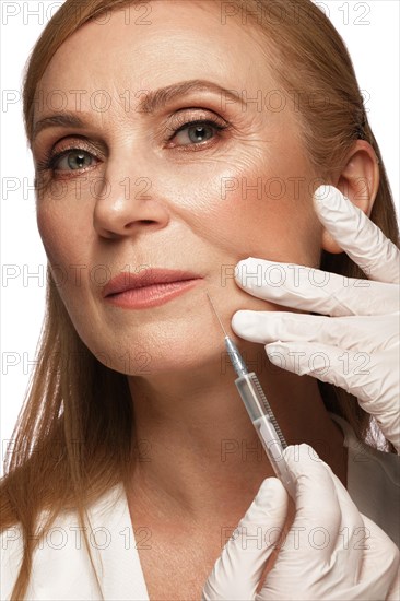 Portrait of a beautiful elderly woman in a white shirt with classic makeup and blond hair with syringe in her hands