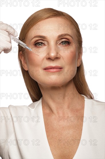 Portrait of a beautiful elderly woman in a white shirt with classic makeup and blond hair with syringe in her hands