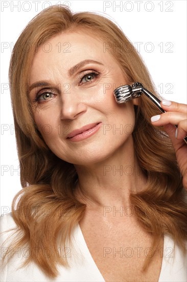 Portrait of a beautiful elderly woman in a white shirt with classic makeup and blond hair with massage tools in hand