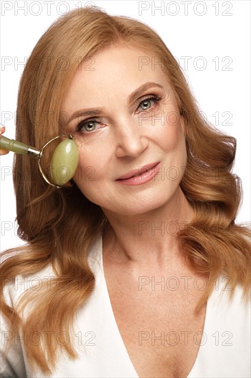 Portrait of a beautiful elderly woman in a white shirt with classic makeup and blond hair with massage tools in hand