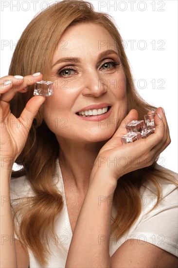 Portrait of a beautiful elderly woman in a white shirt with classic makeup and blond hair with ice in hand