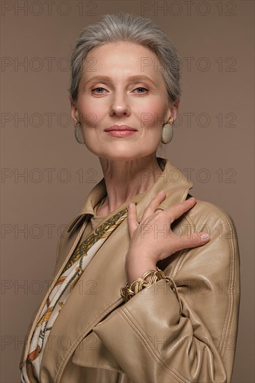 Portrait of a beautiful elderly woman in a beige raincoat with classic makeup and gray hair