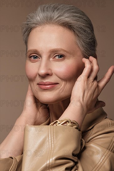 Portrait of a beautiful elderly woman in a beige raincoat with classic makeup and gray hair