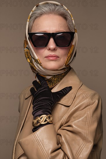 Portrait of a beautiful elderly woman in a beige raincoat with classic makeup and gray hair