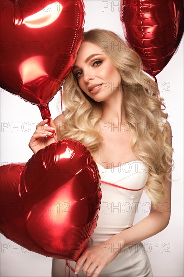 Sexy woman in white dress and balloons with hearts posing in the studio on Valentine's Day