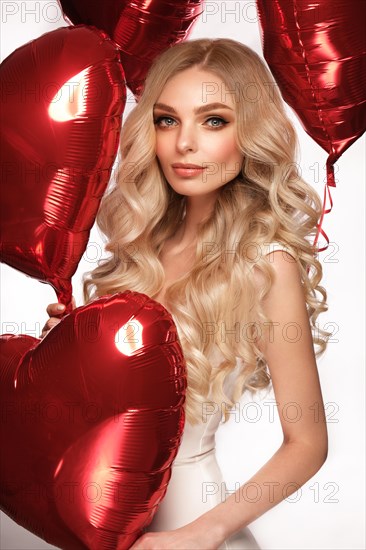 Sexy woman in white dress and balloons with hearts posing in the studio on Valentine's Day