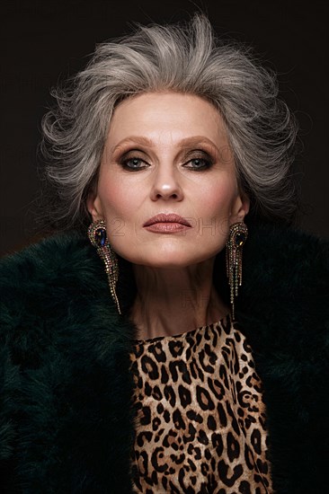 Portrait of a beautiful elderly woman in a leopard blouse and fur coat with classic makeup and gray hair