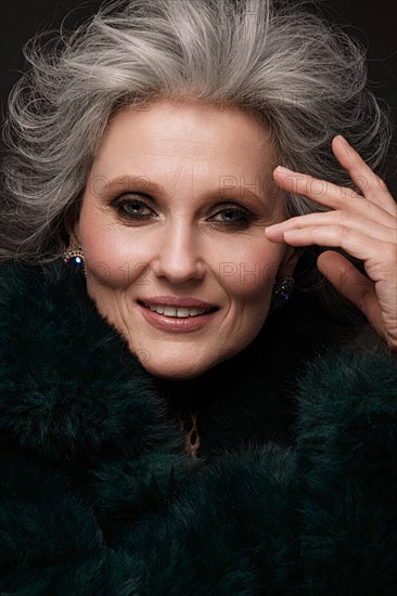 Portrait of a beautiful elderly woman in a leopard blouse and fur coat with classic makeup and gray hair