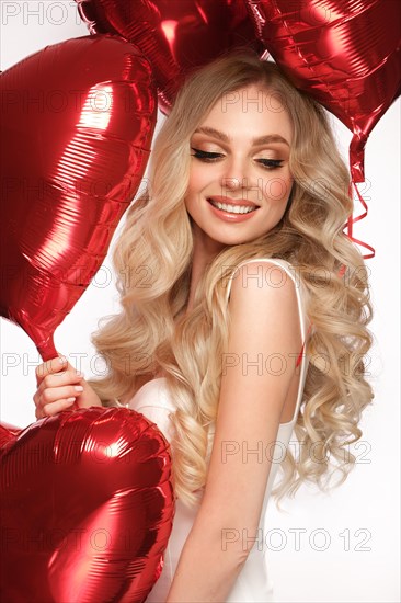 Sexy woman in white dress and balloons with hearts posing in the studio on Valentine's Day