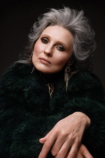 Portrait of a beautiful elderly woman in a leopard blouse and fur coat with classic makeup and gray hair