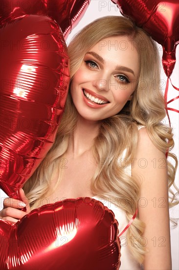 Sexy woman in white dress and balloons with hearts posing in the studio on Valentine's Day