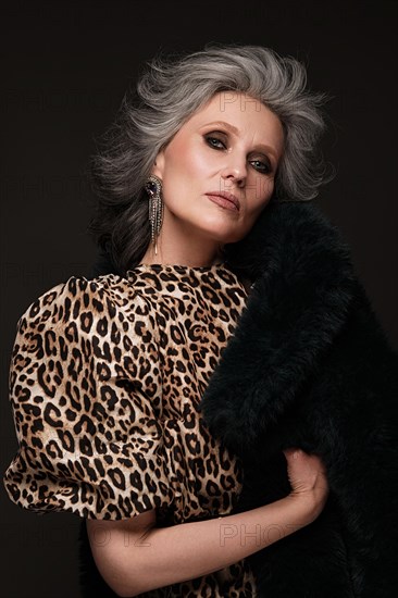 Portrait of a beautiful elderly woman in a leopard blouse and fur coat with classic makeup and gray hair