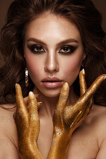Beautiful girl with bright fashionable make-up and gold hands and accessories. Beauty face. Photo taken in the studio