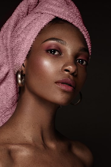 Beautiful black woman with a pink towel on her head and classic makeup. Beauty face. Photo taken in the studio