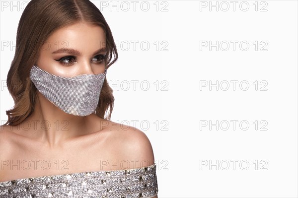 Portrait of a beautiful woman in a silver mask with rhinestones and classic makeup. Mask mode during the covid pandemic