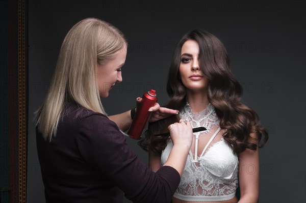 Hairdresser and beautiful brunette girl with a perfectly curls hair and classic make-up. Beauty face. Picture taken in the studio