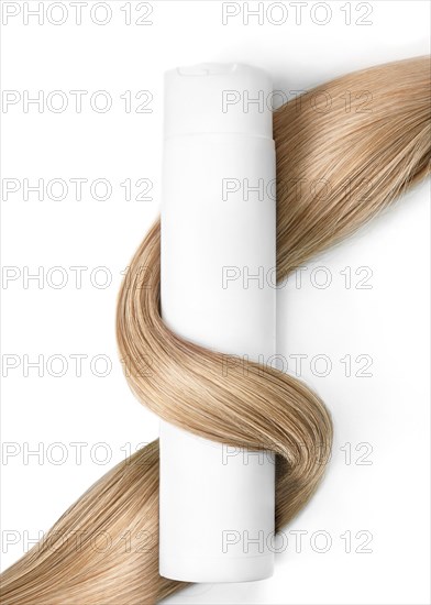 A strand of blond hair with a bottle of shampoo on a white background. Close-up