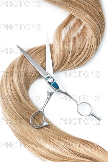 A strand of blond hair with scissors on a white background. Close-up