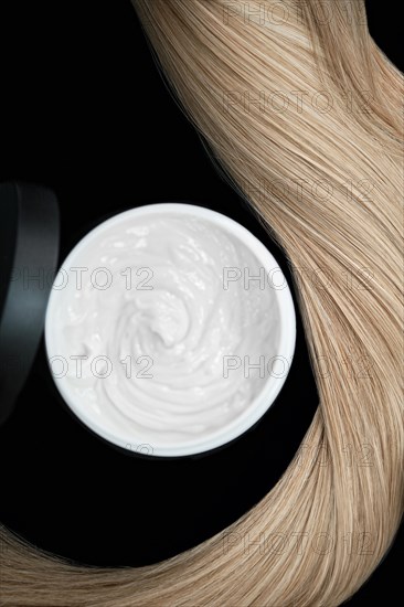 A strand of blond hair with hair balm on a black background. Close-up