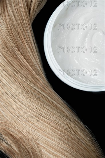 A strand of blond hair with hair balm on a black background. Close-up