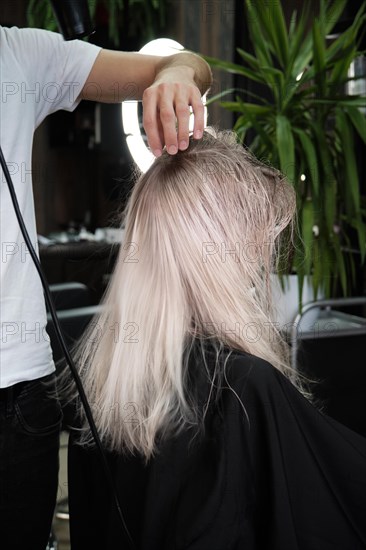 Young woman in a hairdressing salon dyes her hair blond and dries hair