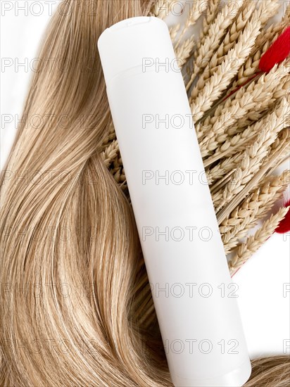 A strand of blond hair with a bottle of shampoo on a white background. Close-up