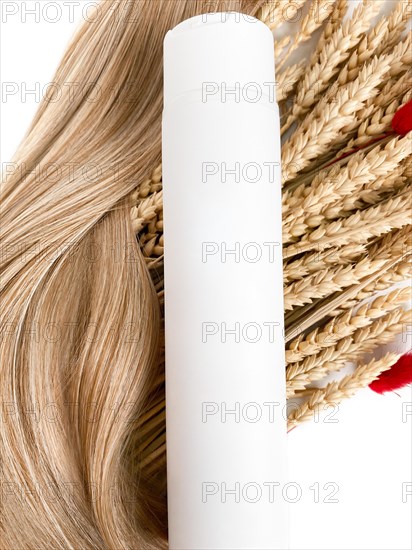 A strand of blond hair with a bottle of shampoo on a white background. Close-up